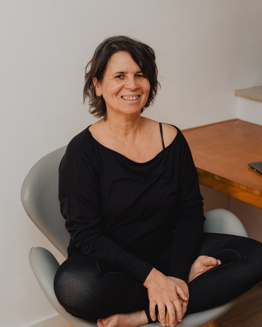 Portrait de Raquel Devillé, thérapeute somatique, assise en tailleur dans son fauteuil de consultation